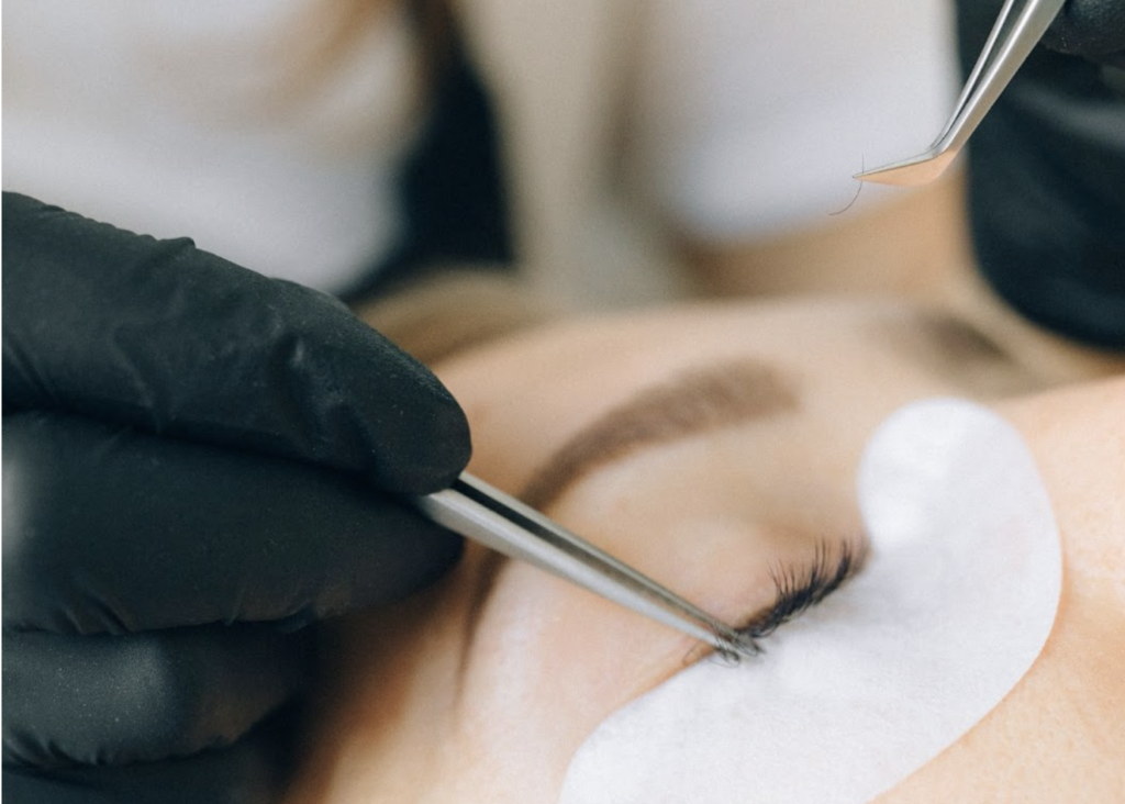 Eyelash technician places and eyelash extension on top of client's eyelashes