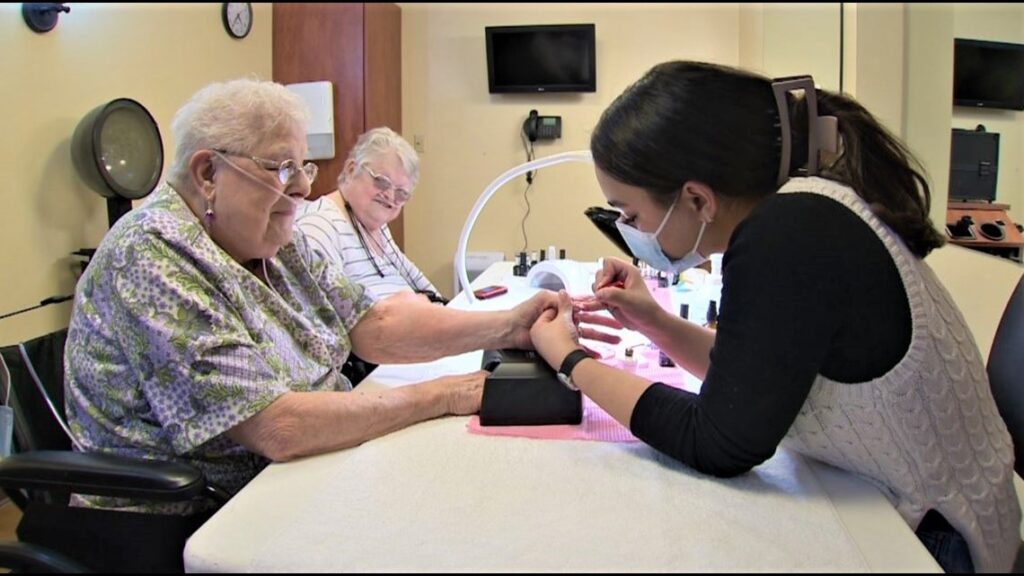 Atelier student, Marielle Smith, paints the nails of two senior women at the Good Samaritan Society