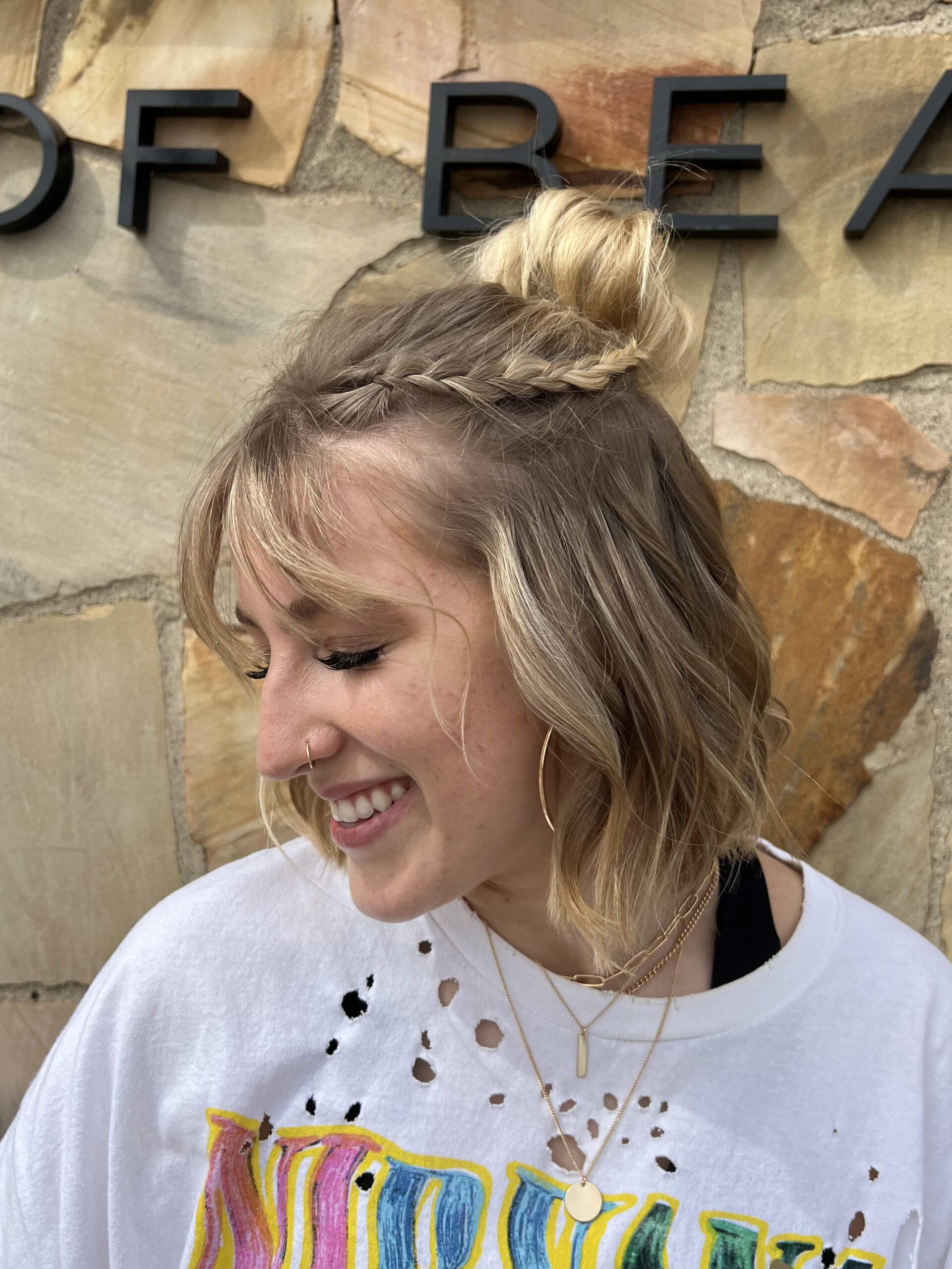 Prom or wedding hairstyle for short hair. Chin length lob is pulled into a half-up, half-down bun with a small braid. Model is looking left and smiling.