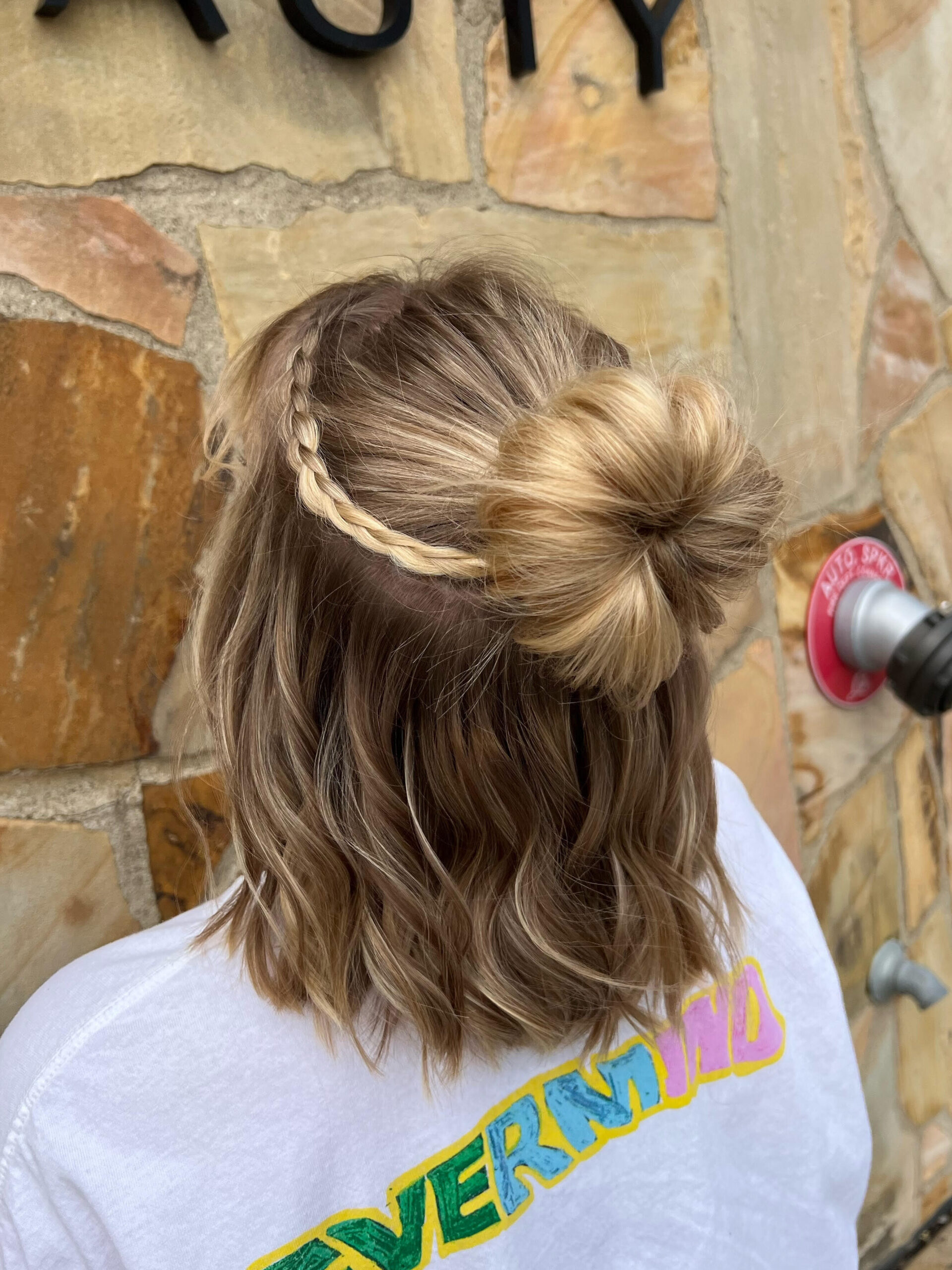 Prom or wedding hairstyle for short hair. Chin length lob is pulled into a half-up, half-down bun with a small braid. Model is facing away.