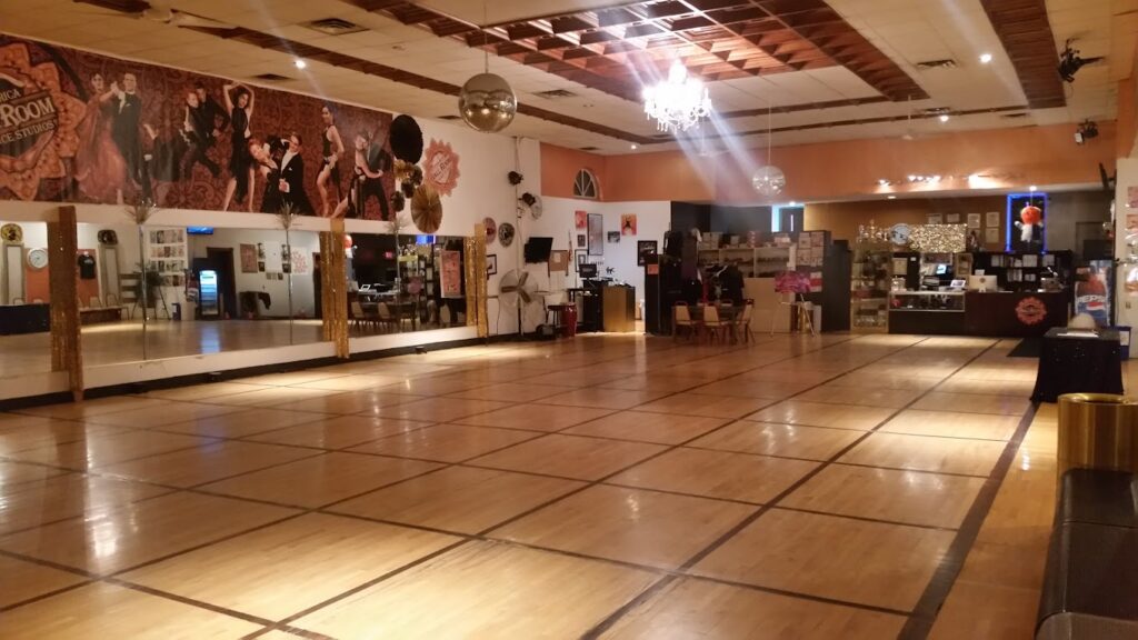 A dance studio at Costa Rica Ballroom illuminated by a chandelier and disco balls, featuring pictures of dancers on the wall.