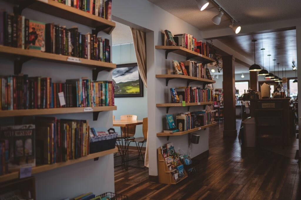 A moody, cozy view of book shelves lining the wall in front of café tables and the coffee station in the background of Cream & Amber bookstore and coffee shop in Hopkins, MN.