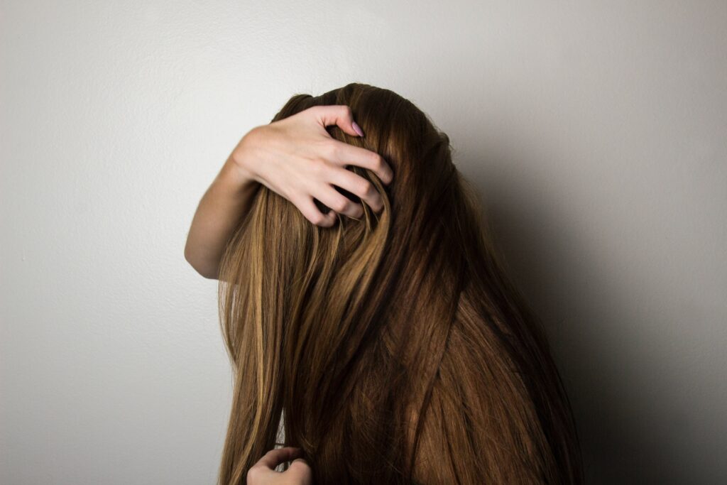 Long haired individual hides face behind hair and grabs head with right hand