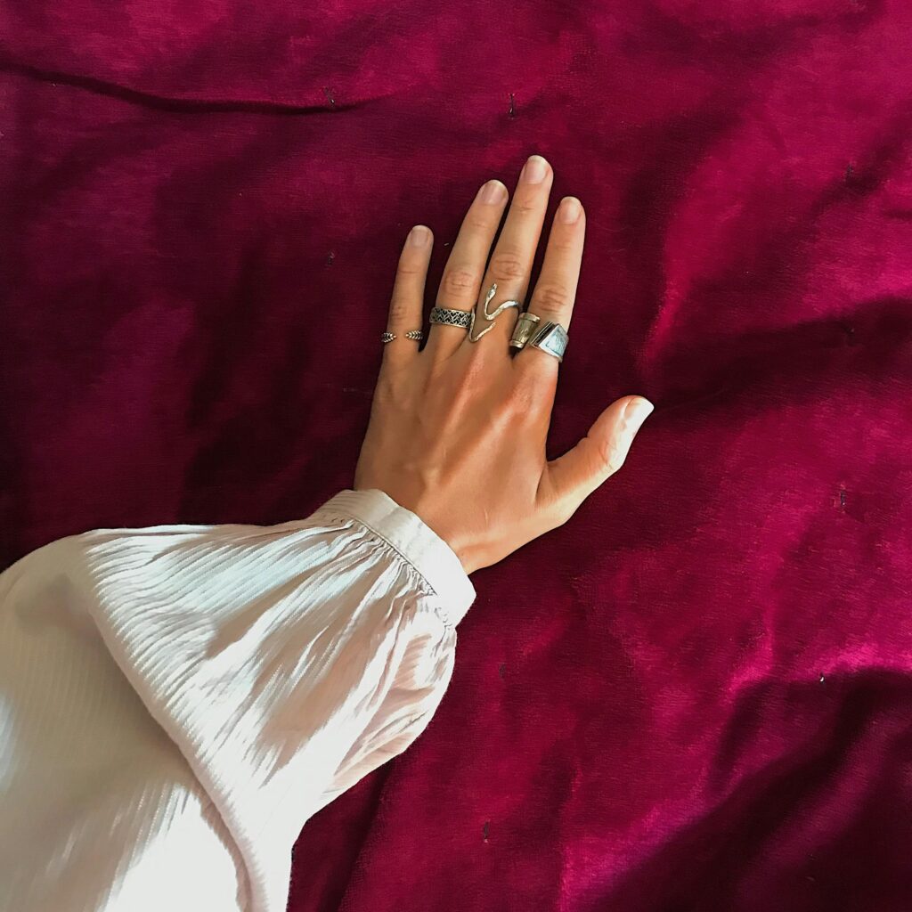 A hand full of silver rings rests on red fabric and displays a buff and shine manicure