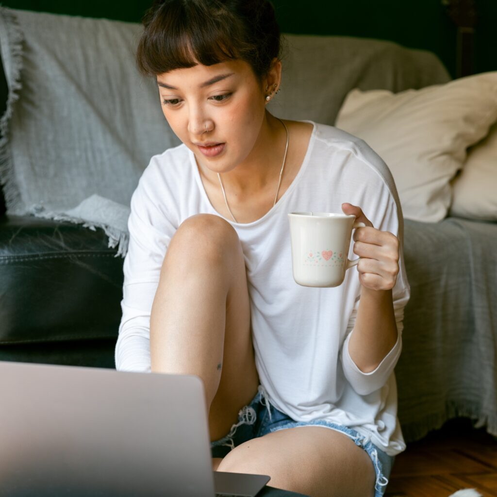 Woman sits on the ground with a mug and searches the computer to find out how to renew an expired license