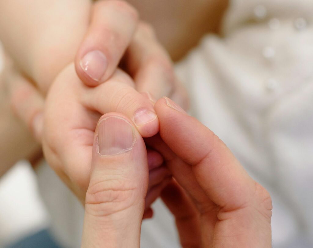 An adult hand uses its thumb and pointer finger to gently pinch a baby thumb to show the difference between adults nails and baby nails