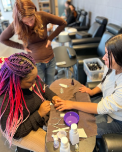 Atelier student manicures another student's nails while an instructor watches on