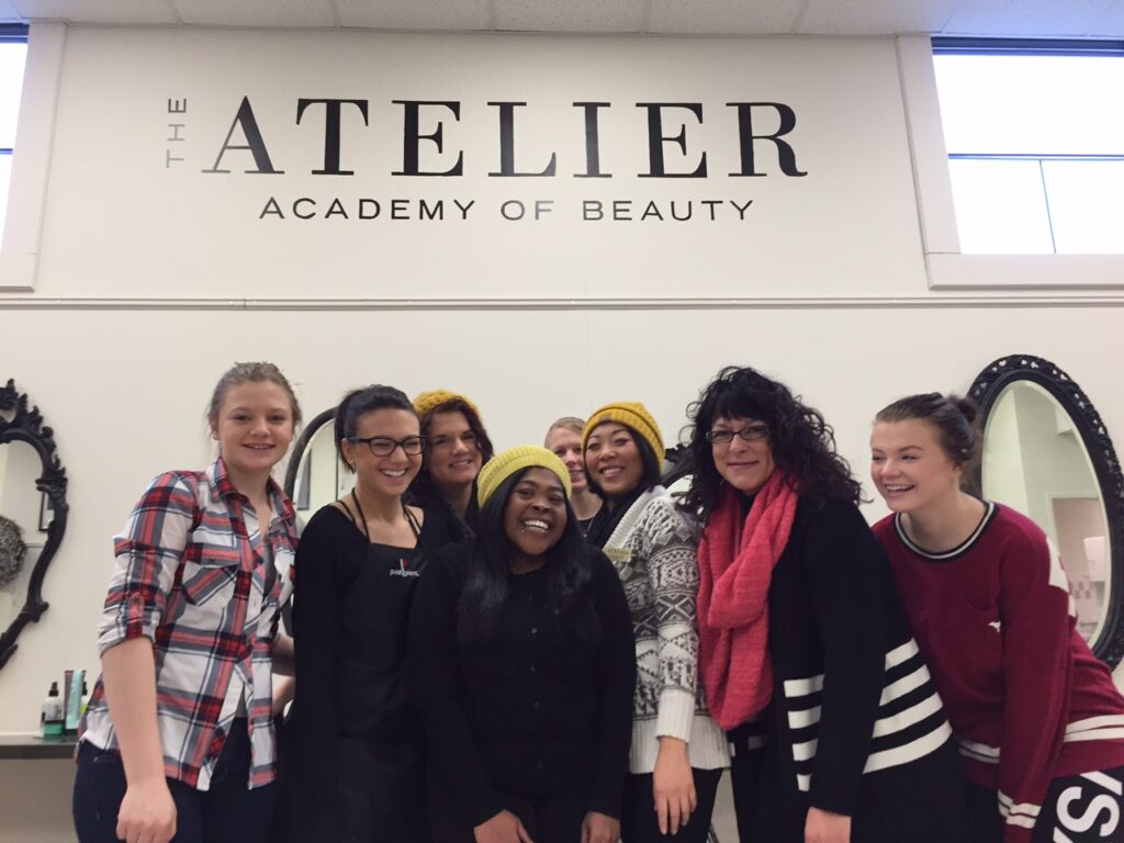 A group of students smiles and laugh at the camera in front of a wall of the old Atelier building