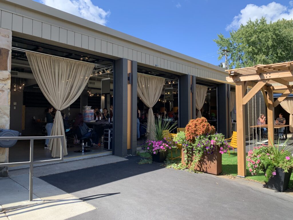 A view of the outside of the Atelier Academy, showcasing large open doors that let in natural sunlight and air