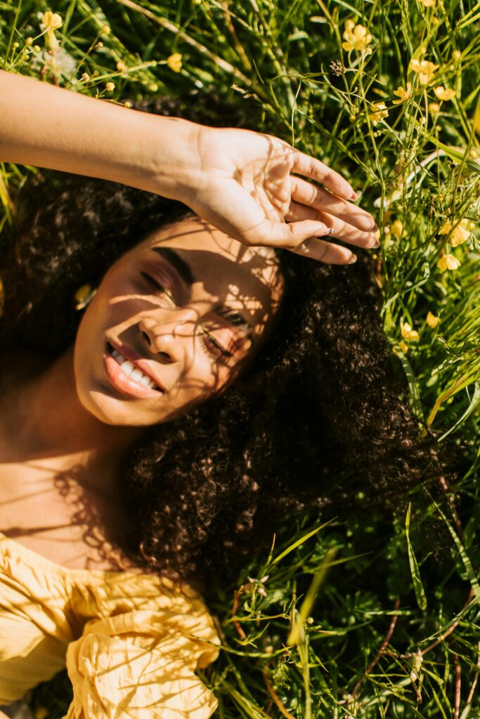 Woman smiles as she lays in a field of spring flowers with the sun shining on her face
