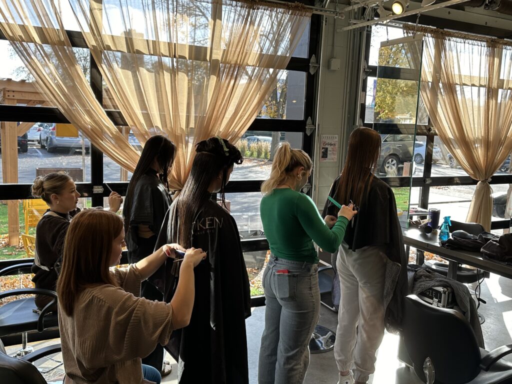 Students at the Atelier cut hair in the bright light streaming in large garage windows