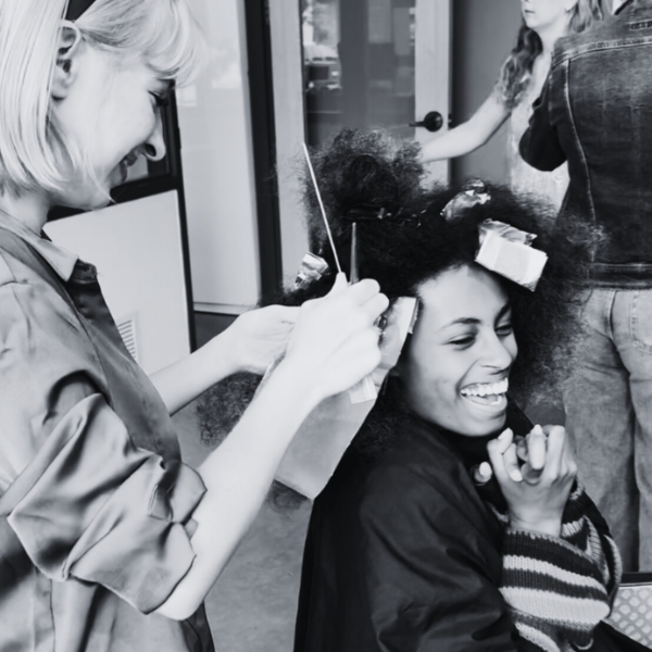 A client smiles and laughs broadly as a smiling student applies foils to their hair.