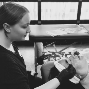 Student brushes through client's eyebrows with a spoolie